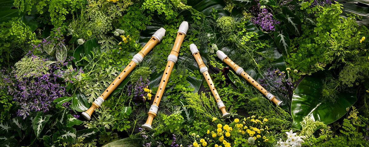 Four Yamaha recorders made of bioplastic placed on a bed of plants.