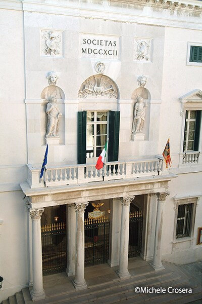 Exterior of Teatro Malibran in Venice, featuring a historic façade with columns, flags, and classical architectural details.